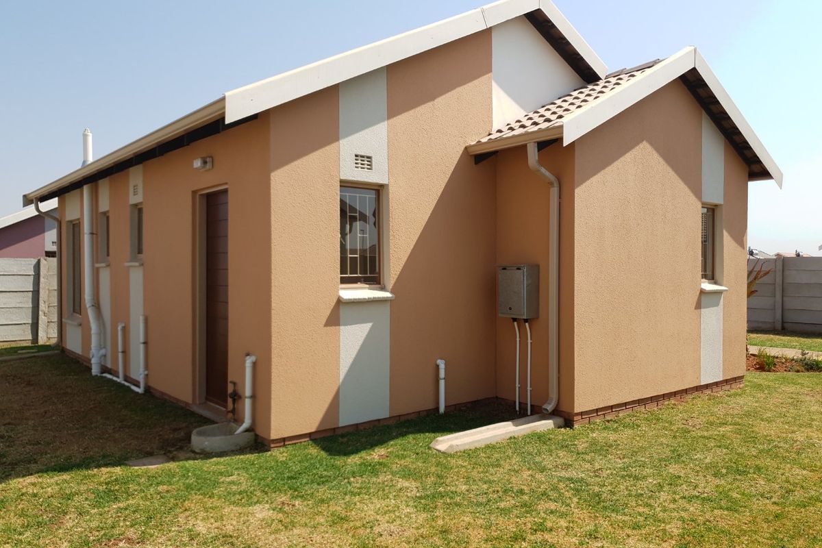 Rear view of the house featuring a tiled roof, textured plaster exterior, external lighting, and a gas geyser, set within a private garden area.