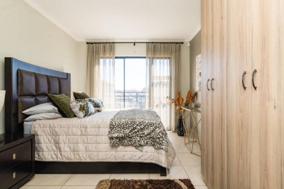 A well-maintained bedroom featuring built-in cupboards, tiled flooring, and a sliding glass door providing natural light and access to the exterior.