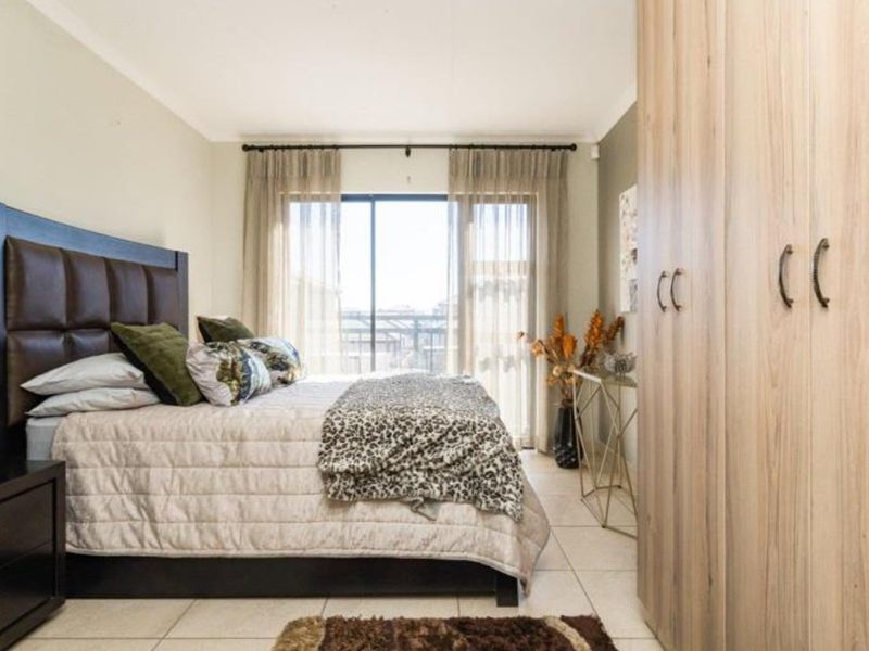 A well-maintained bedroom featuring built-in cupboards, tiled flooring, and a sliding glass door providing natural light and access to the exterior.