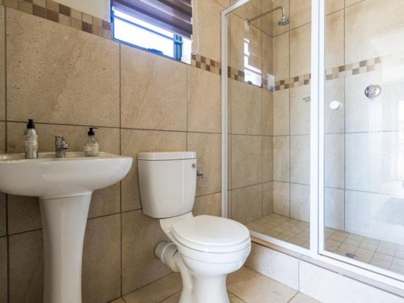 A functional bathroom featuring a pedestal basin, toilet, and a glass-enclosed shower with neutral wall and floor tiling.
