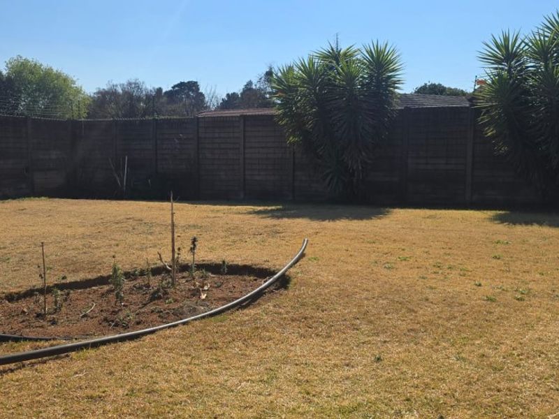 A spacious backyard featuring a large lawn area enclosed by a precast concrete boundary wall with integrated electric fencing.