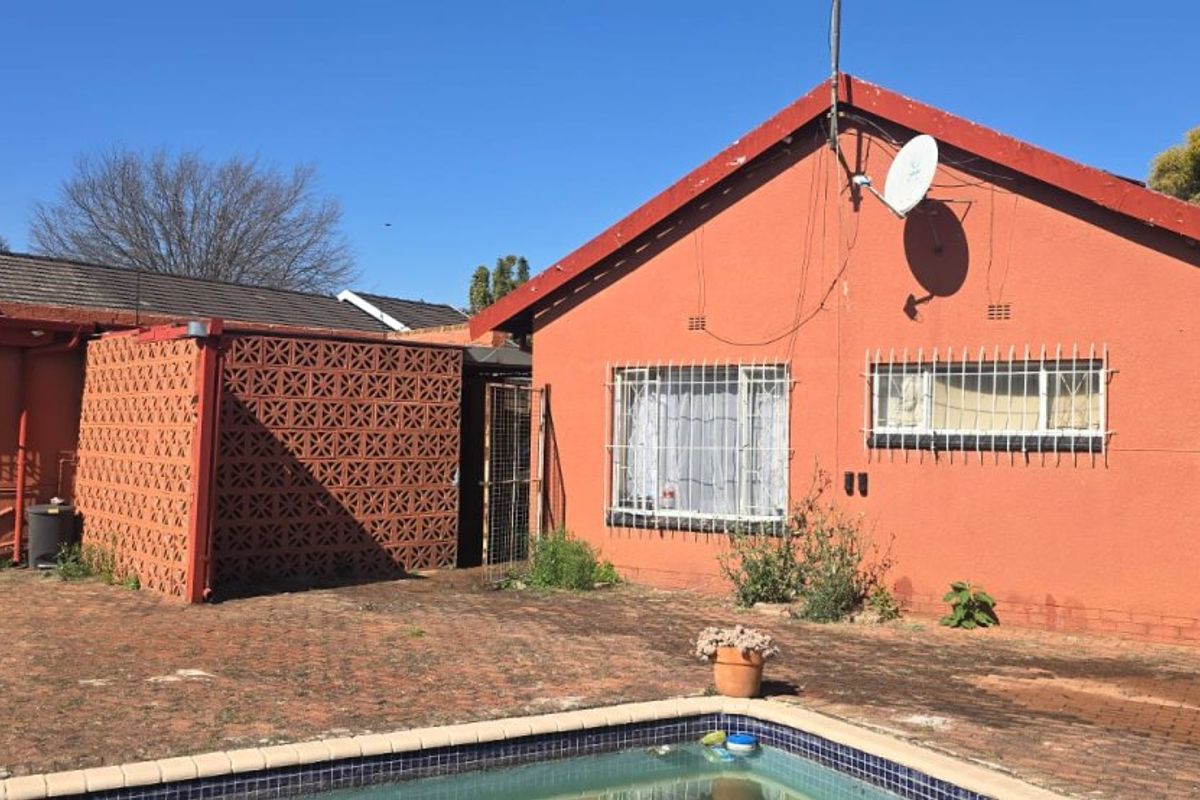Rear exterior view of the house featuring a swimming pool, brick paved patio area, and security bars on windows.