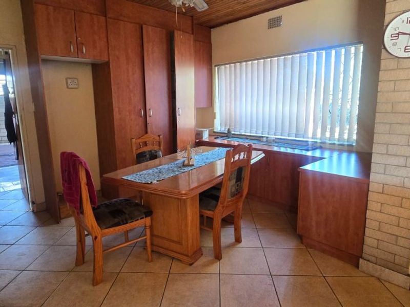 Dining area featuring built-in timber cabinetry, tiled flooring, and a brick feature wall, offering a dated aesthetic with potential for modernization.