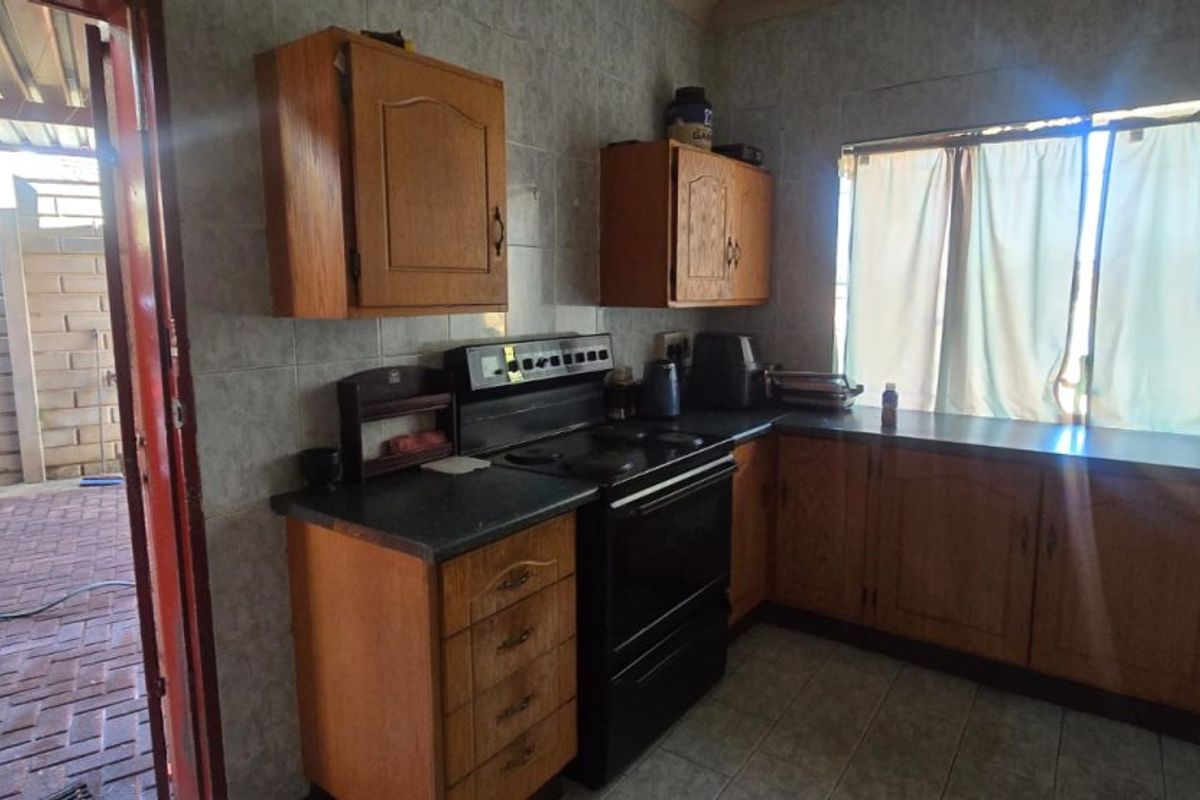 A functional kitchen featuring wooden cabinetry, tiled wall finishes, and a freestanding stove, with direct access to an outdoor paved area.