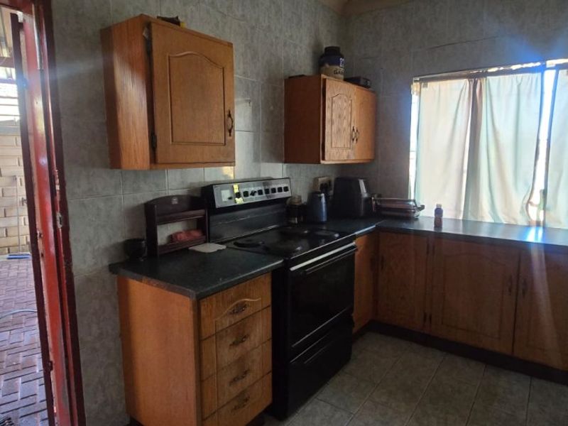 A functional kitchen featuring wooden cabinetry, tiled wall finishes, and a freestanding stove, with direct access to an outdoor paved area.