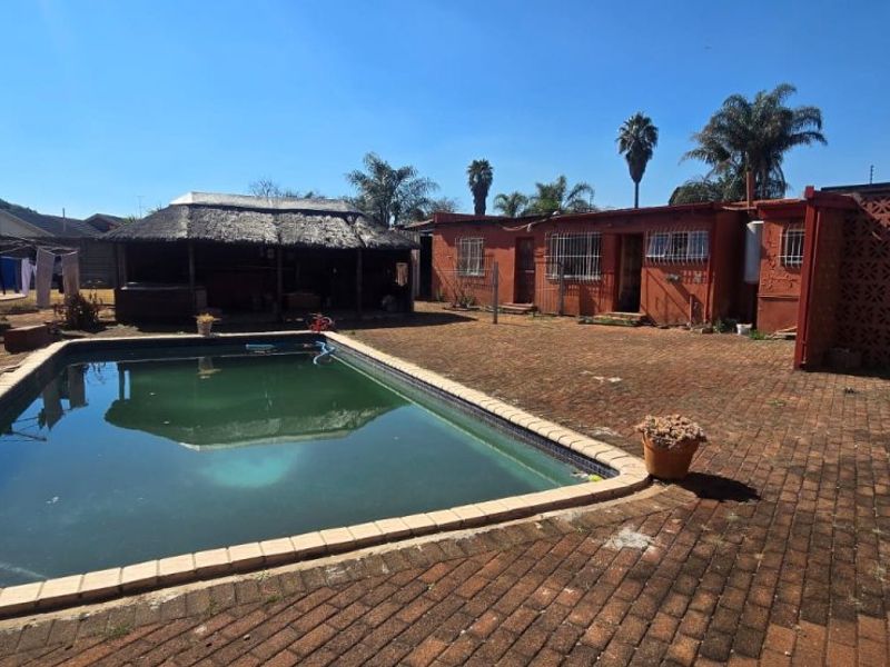 Outdoor pool area featuring a swimming pool, brick paving, and a thatched lapa structure, set within a private backyard space.