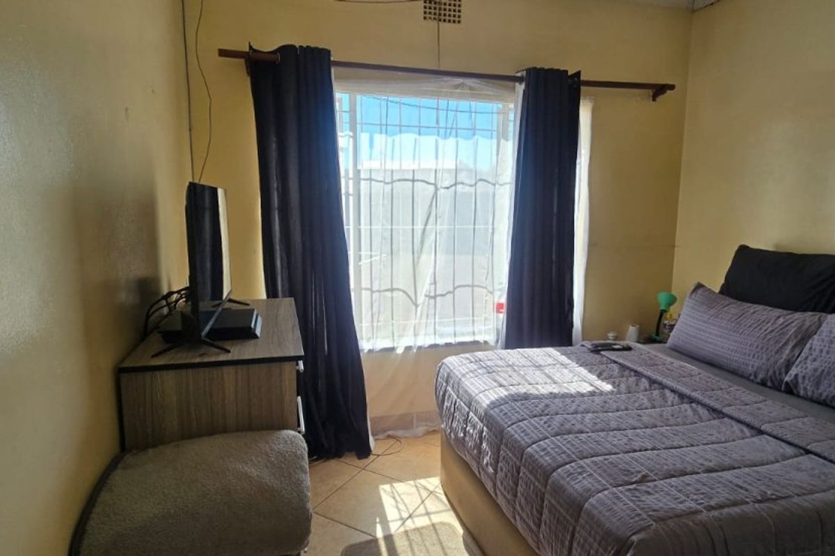 A bedroom featuring tiled flooring and a window with security bars. The space requires cosmetic updates to the wall finishes.