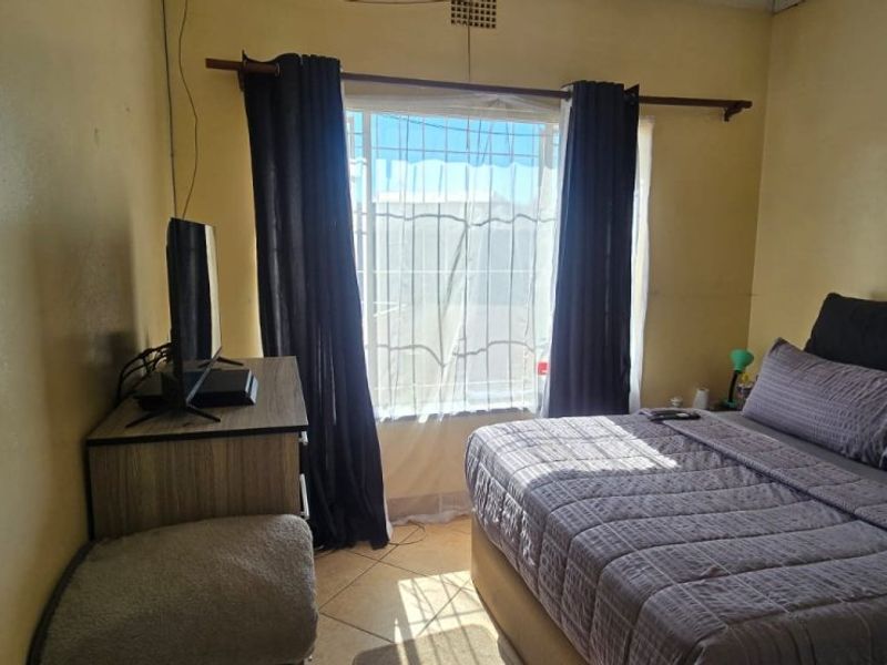 A bedroom featuring tiled flooring and a window with security bars. The space requires cosmetic updates to the wall finishes.