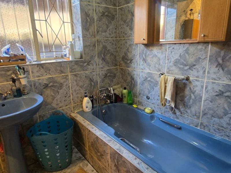 A dated bathroom featuring blue sanitaryware, wall-mounted cabinetry, and patterned wall tiles, offering potential for a modern renovation.