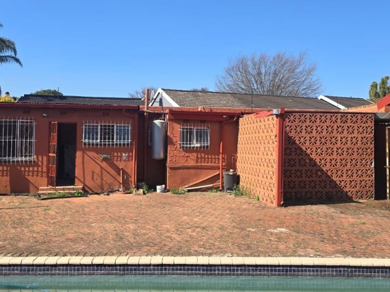 Rear exterior view featuring a swimming pool, brick paved patio area, and traditional brick building facade with security bars.