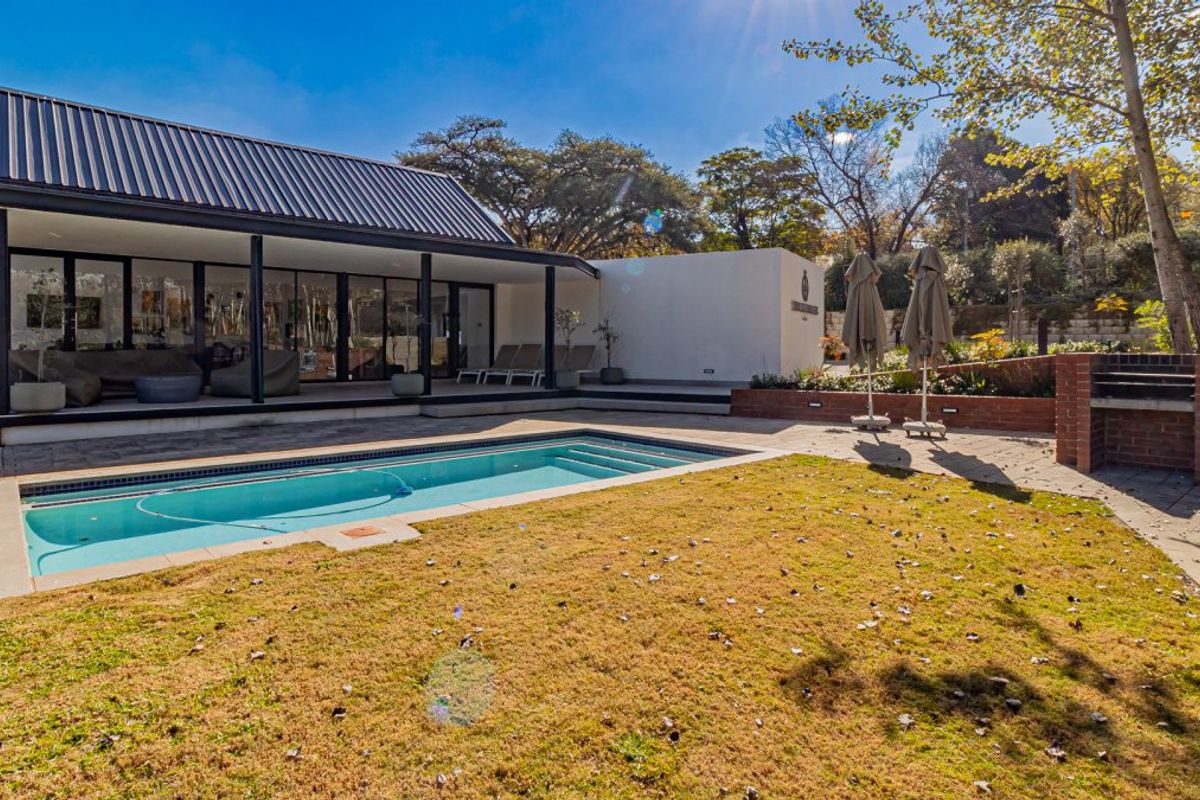 A well-maintained outdoor entertainment area featuring a swimming pool, paved patio, and a built-in brick braai, perfect for outdoor living.