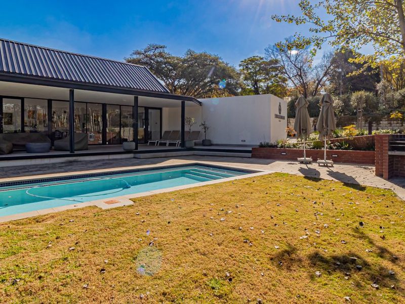 A well-maintained outdoor entertainment area featuring a swimming pool, paved patio, and a built-in brick braai, perfect for outdoor living.