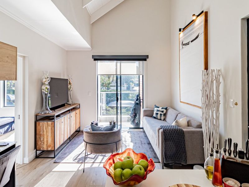 Bright open-plan living area featuring vaulted ceilings, laminate flooring, and direct access to a private balcony through sliding glass doors.
