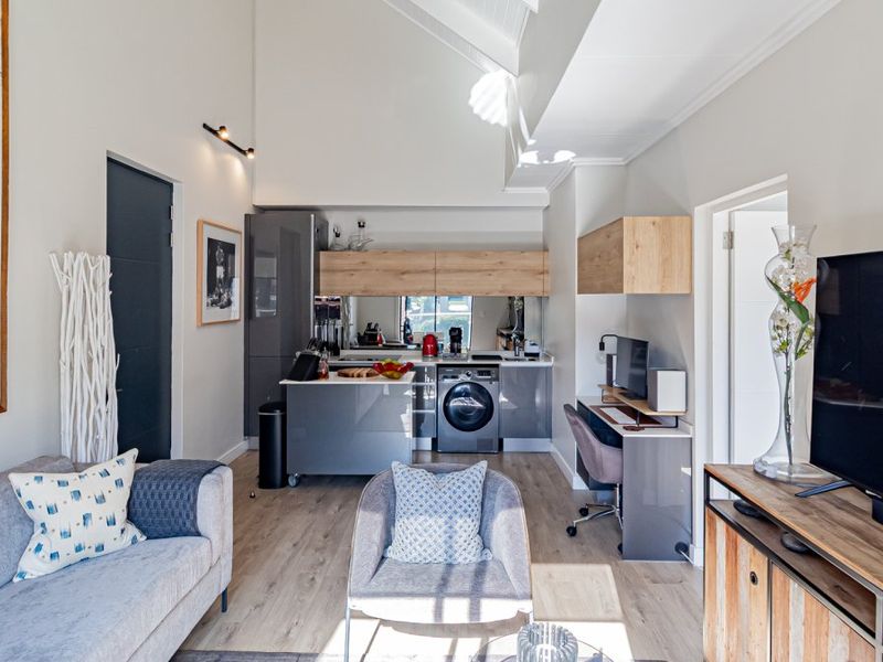 Modern open-plan living area featuring high vaulted ceilings, laminate flooring, and a compact kitchen with integrated appliances and sleek cabinetry.