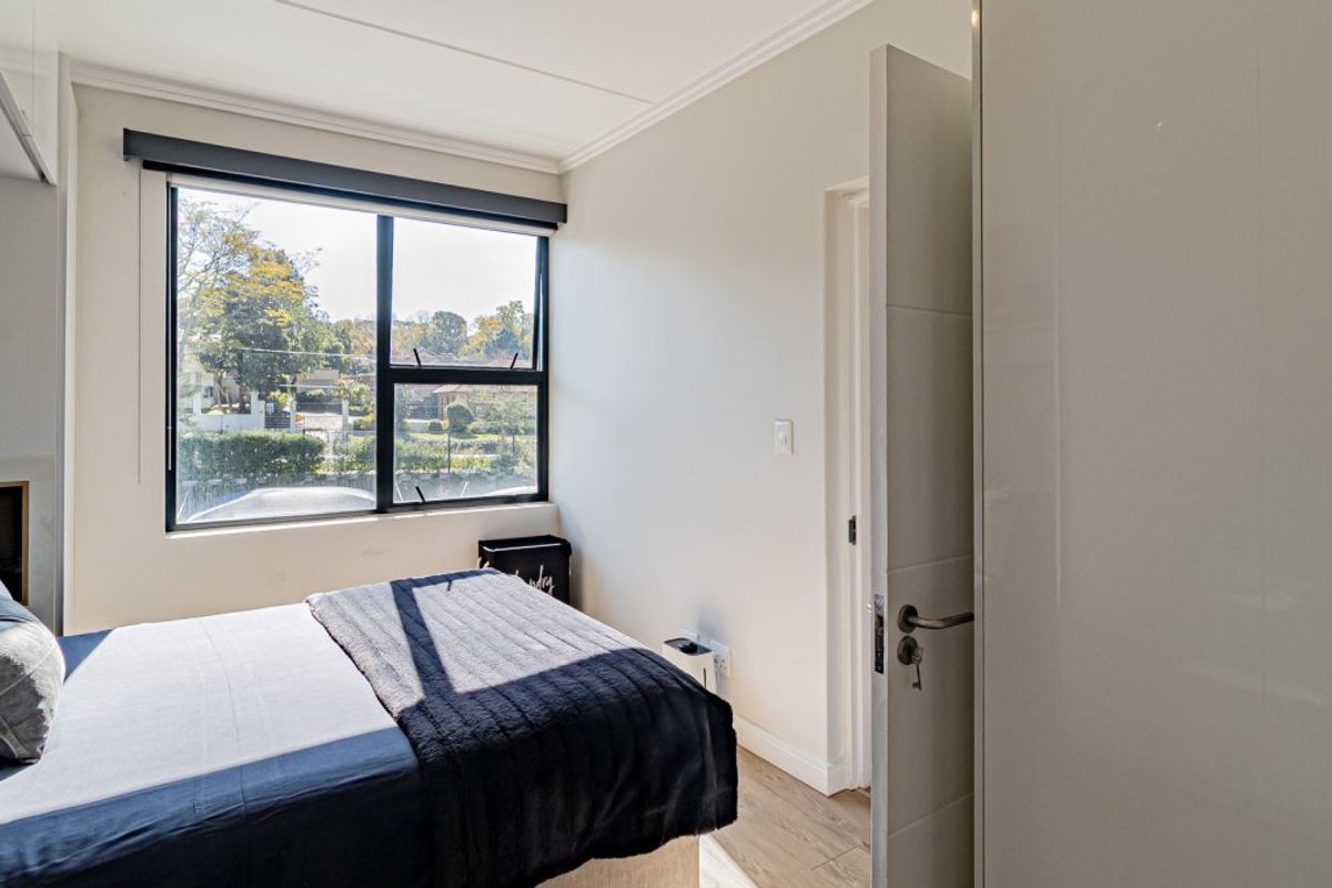 A bright bedroom featuring laminate flooring, a built-in wardrobe, and large windows providing natural light and a pleasant outdoor view.