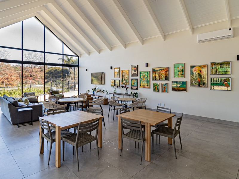 Spacious open-plan living area featuring high vaulted ceilings with exposed rafters, large floor-to-ceiling windows, and modern tiled flooring.
