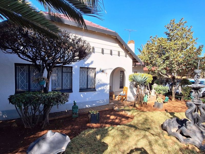 Front elevation of a residential house featuring a tiled roof, arched entrance, and security bars on the windows, set within a landscaped garden.