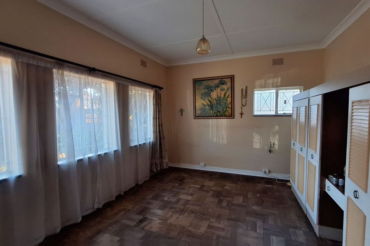 A bedroom featuring parquet flooring, built-in cupboards, and large windows with security bars, offering a functional space with classic finishes.