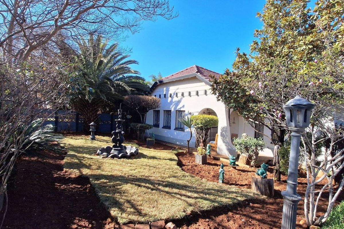 A well-maintained rear garden featuring a central fountain, mature landscaping, and a charming house exterior with arched architectural details and tiled roofing.