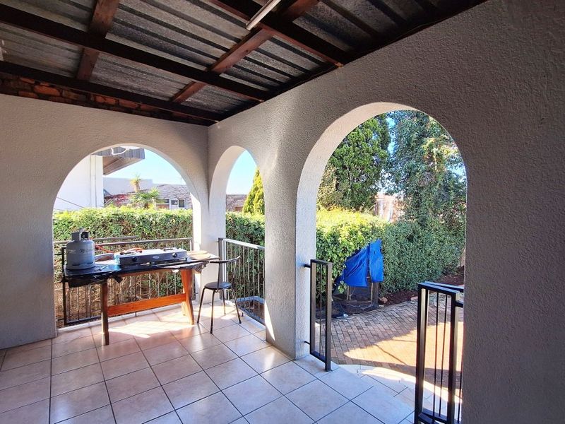 A covered patio area featuring arched masonry openings, tiled flooring, and an exposed beam ceiling, overlooking the garden and pool area.