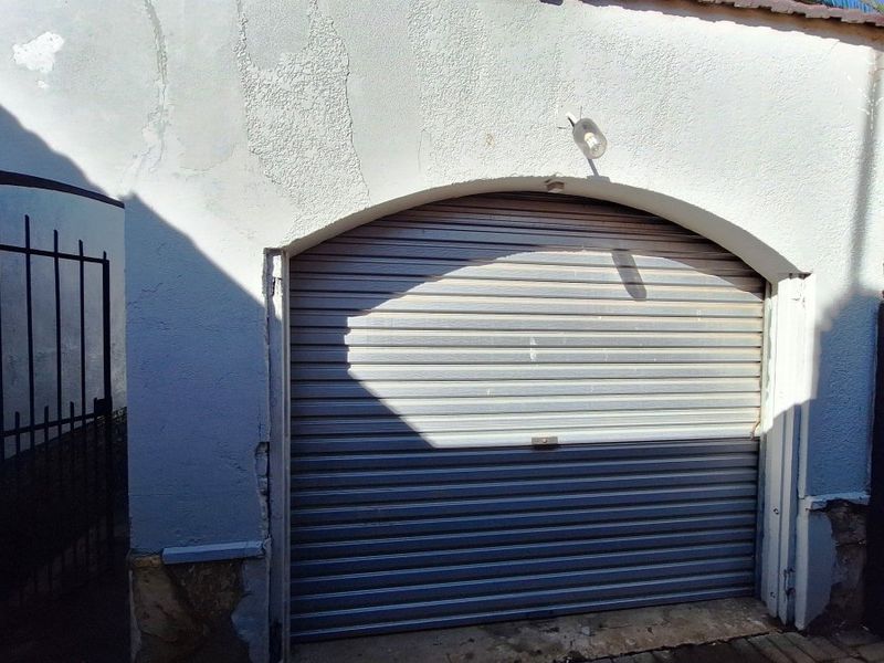 Exterior view of a garage featuring a roller shutter door set within an arched masonry opening, showing signs of weathered exterior finishes.