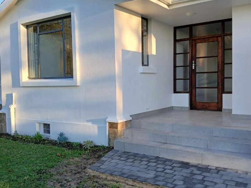 A well-maintained front entrance featuring a timber-framed glass door, tiled steps, and a paved walkway leading to the home.