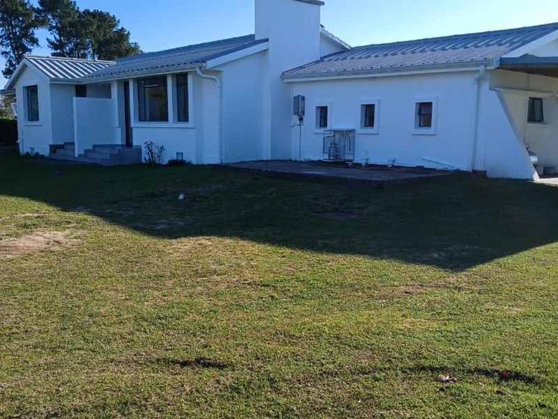 Rear view of a white farmhouse featuring a metal roof, central chimney, and a paved patio area overlooking the surrounding lawn.