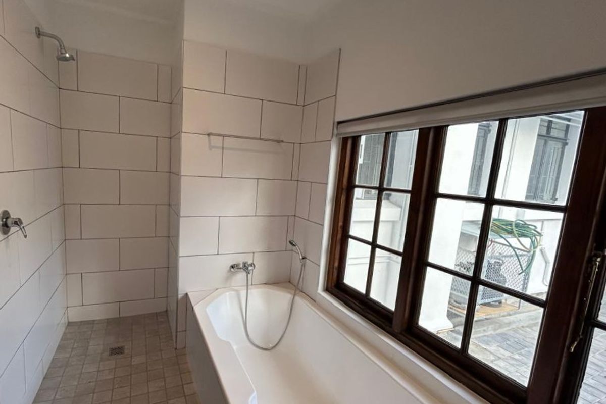 A clean, functional bathroom featuring a walk-in shower, a built-in bathtub, and large windows with timber frames, offering a bright and airy space.