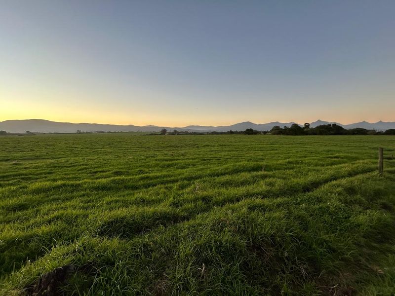 Expansive green pasture land on a farm, featuring a wire fence boundary and scenic mountain views at sunset.