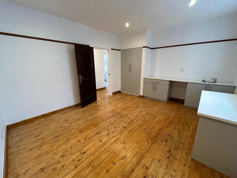 A clean, empty kitchen area featuring polished hardwood flooring, built-in cabinetry with a sink, and a classic tongue and groove ceiling.