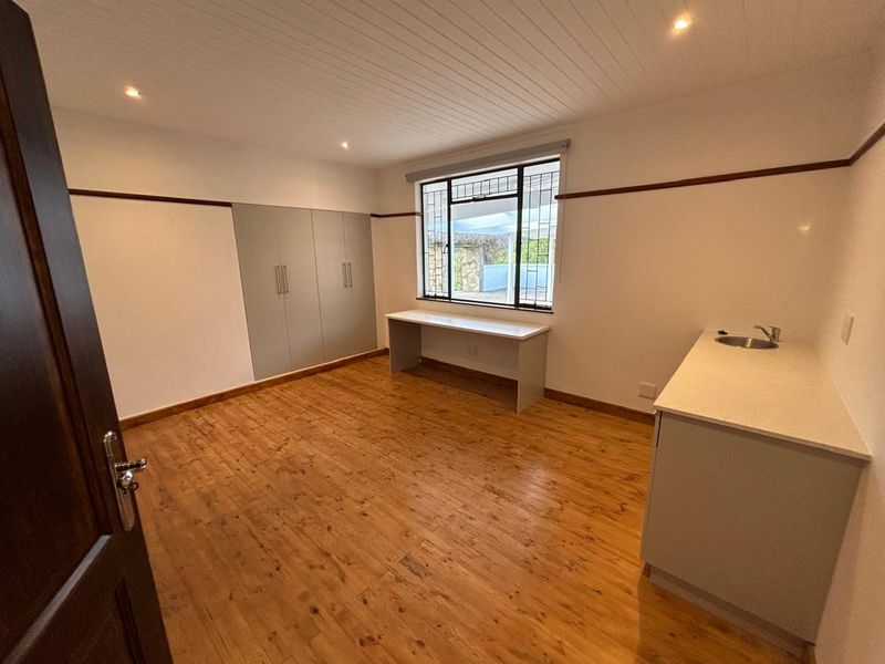 Spacious bedroom featuring timber flooring, built-in cupboards, a built-in desk, and a convenient integrated sink area with recessed lighting.