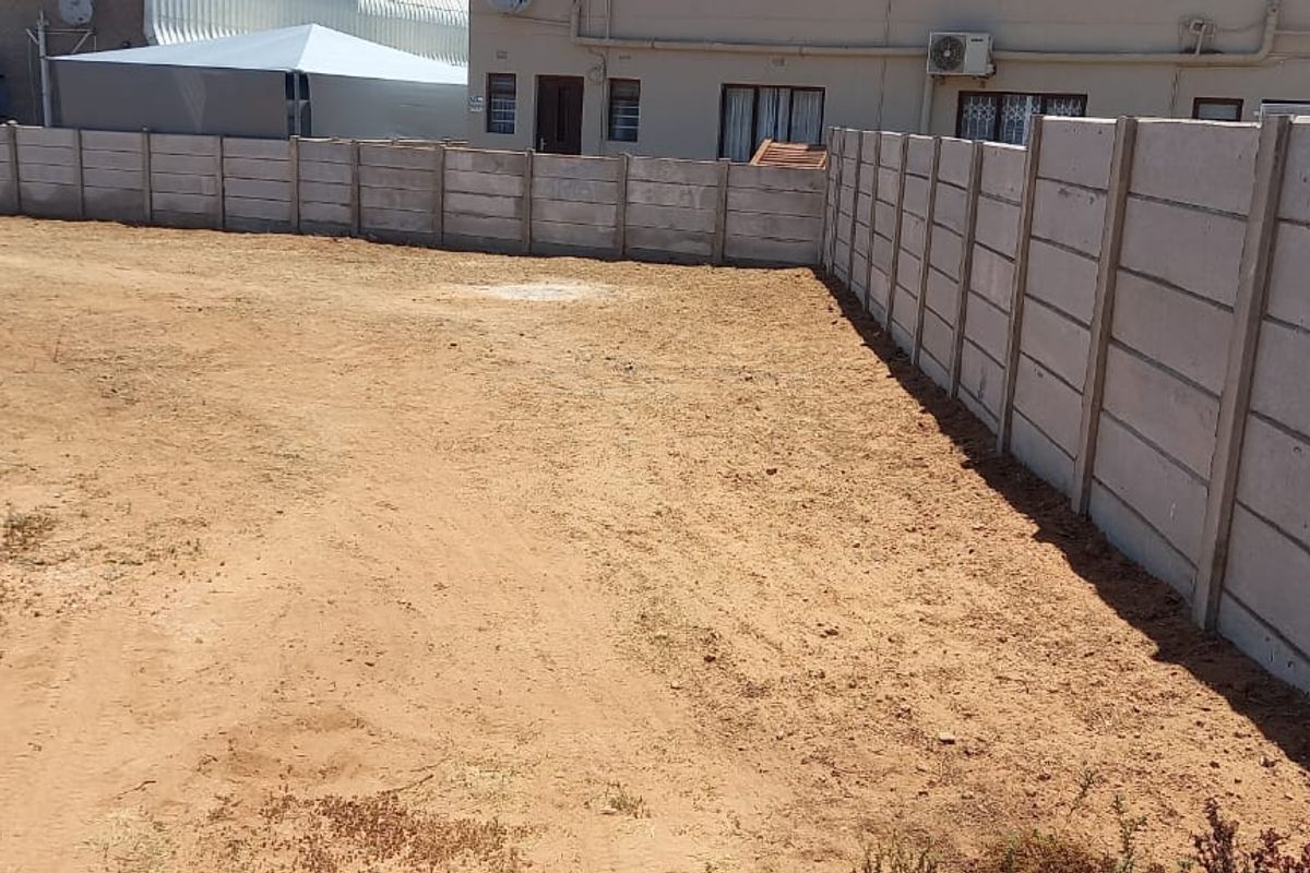 A vacant residential plot featuring a secure precast concrete boundary wall, offering a clear space ready for development.