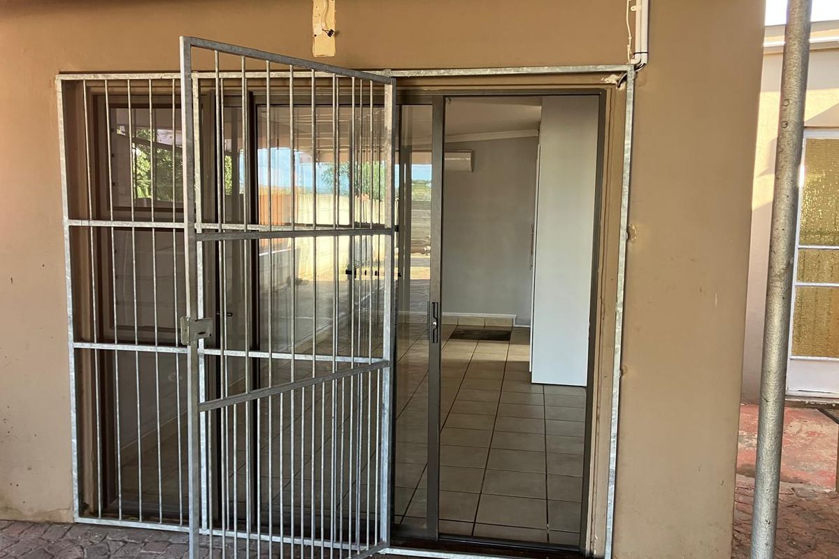 Rear exterior view of an apartment featuring a sliding glass door with a metal security gate and tiled flooring.