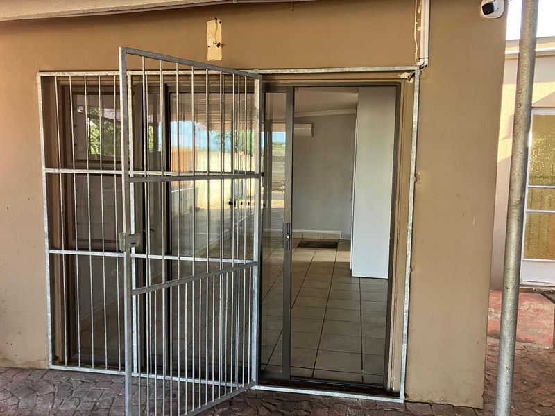Rear exterior view of an apartment featuring a sliding glass door with a metal security gate and tiled flooring.