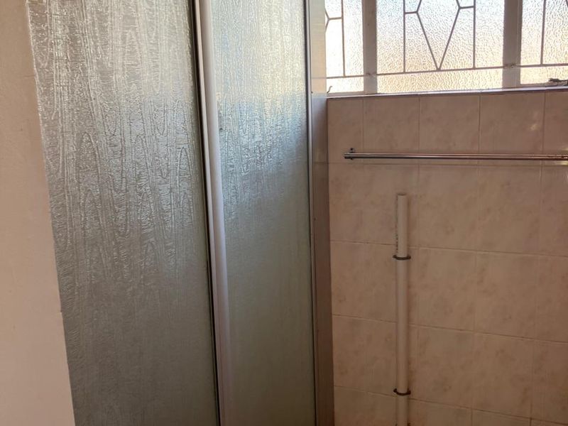 A functional bathroom featuring a shower enclosure, tiled finishes, and a towel rail, with an exposed pipe requiring cosmetic attention.