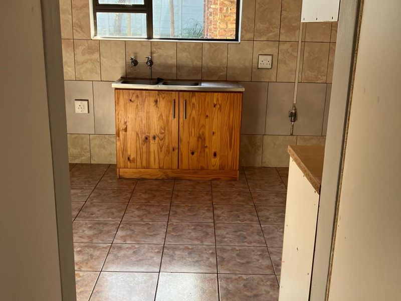A functional kitchen area featuring tiled walls and flooring, a stainless steel sink, and wooden base cabinetry, offering a blank canvas for renovation.