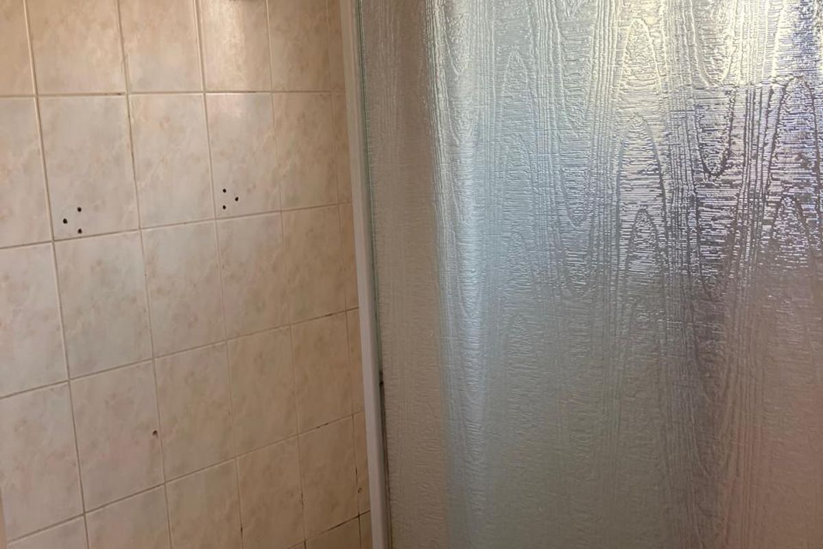 A dated shower stall featuring textured glass doors, tiled walls, and a mosaic-style tiled floor, requiring cosmetic updates.