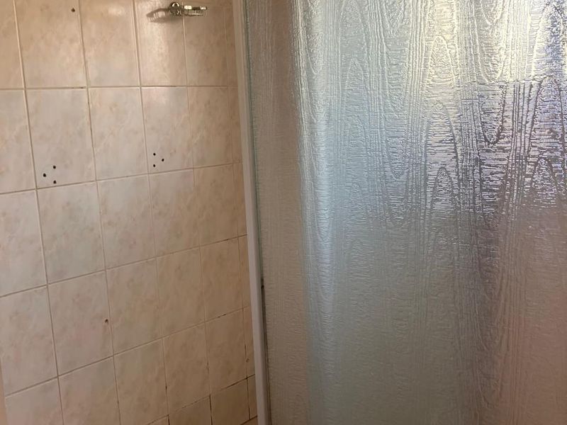 A dated shower stall featuring textured glass doors, tiled walls, and a mosaic-style tiled floor, requiring cosmetic updates.