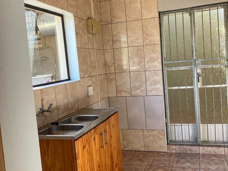 A functional scullery area featuring a double stainless steel sink, wooden cabinetry, tiled surfaces, and a timber ceiling with direct access to an exterior door.