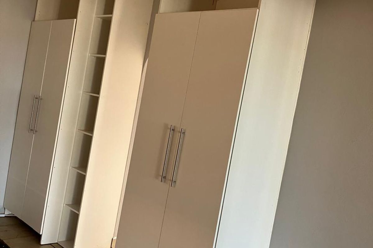 A bedroom featuring white built-in cupboards and neutral tiled flooring, offering a clean and functional storage solution.