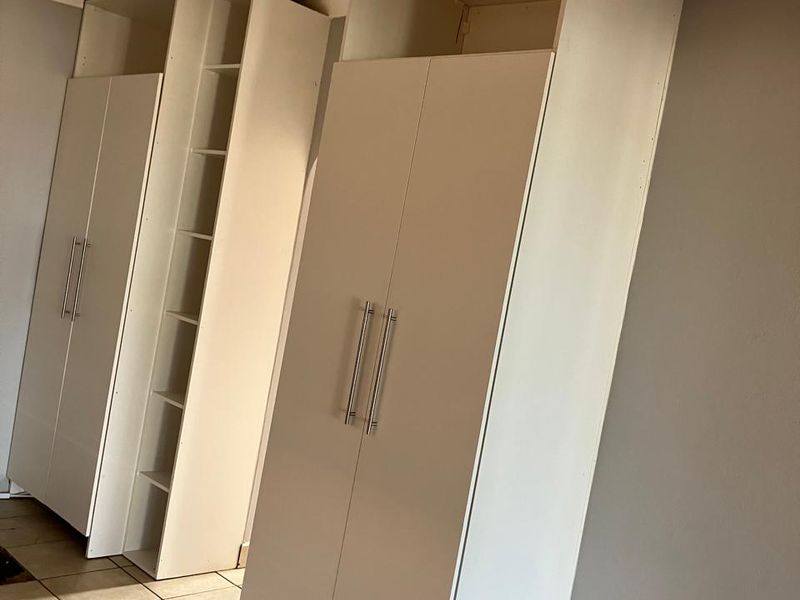 A bedroom featuring white built-in cupboards and neutral tiled flooring, offering a clean and functional storage solution.