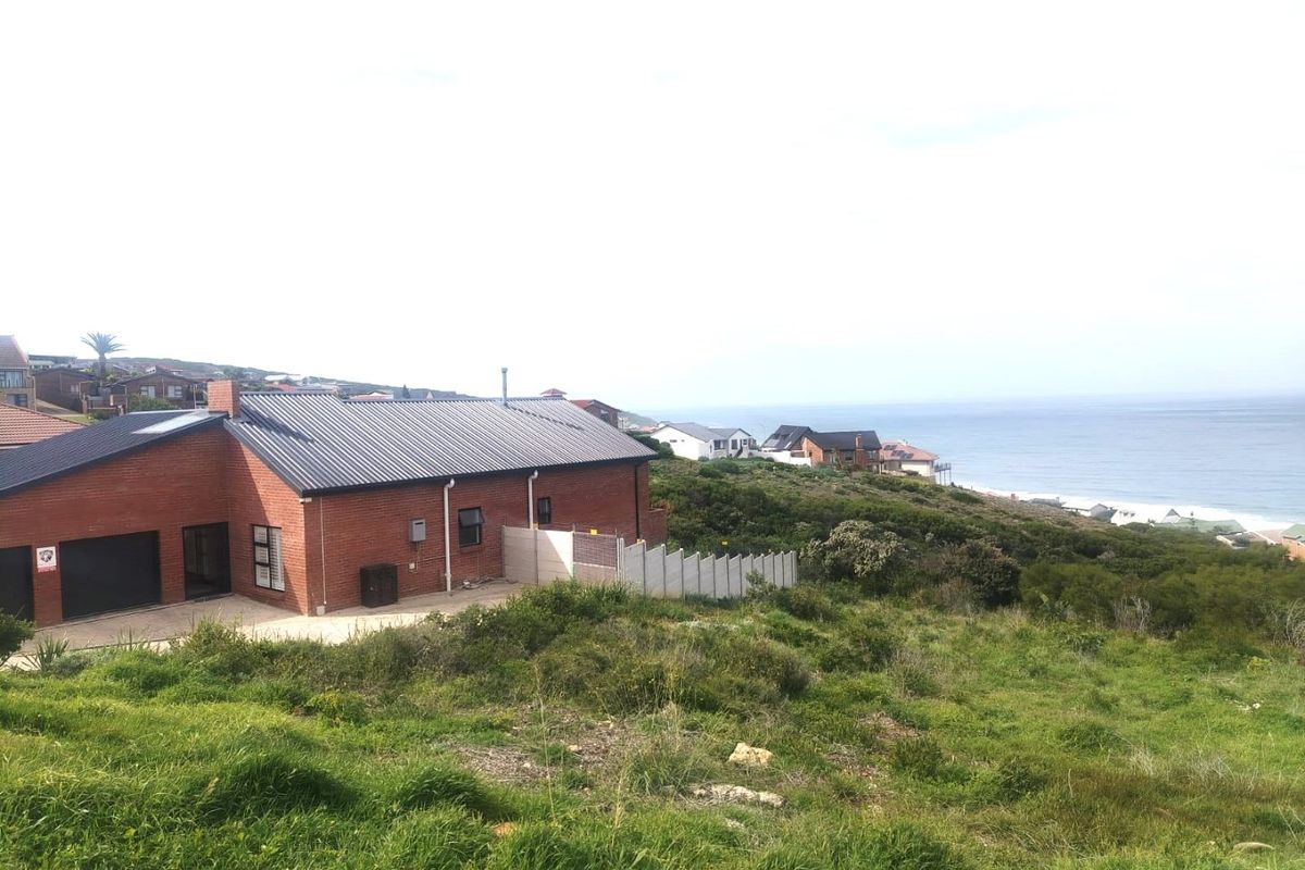 A view of the rear elevation of a brick residential property featuring a metal roof, garage, and concrete boundary wall overlooking the coastline.