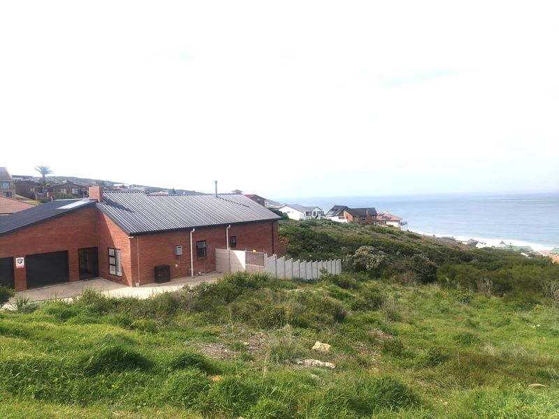 A view of the rear elevation of a brick residential property featuring a metal roof, garage, and concrete boundary wall overlooking the coastline.