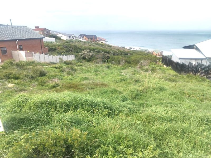 A view of a vacant residential plot featuring sloped terrain with coastal and ocean views in the background.