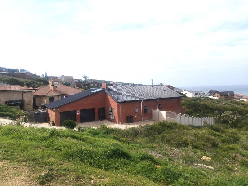 Front view of a modern brick residential property featuring a double garage, metal roofing, and a surrounding concrete boundary wall in a coastal setting.