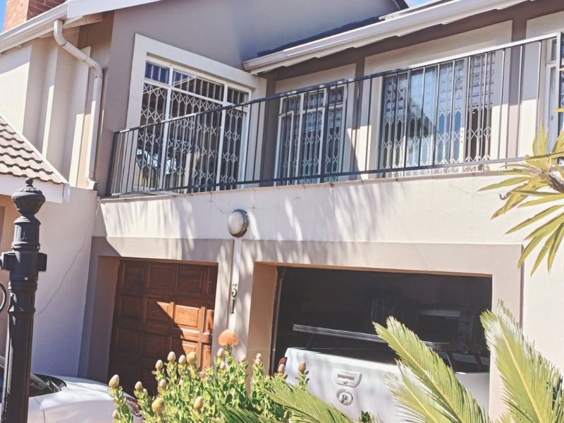 Front elevation of a two-story house featuring a balcony with security railings and a double garage with wooden doors.