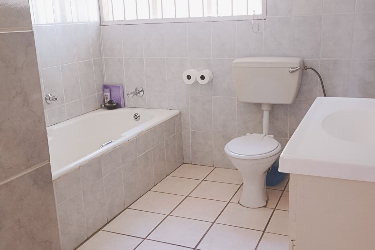 A functional bathroom featuring a built-in bathtub, toilet, and vanity basin with neutral ceramic tiling throughout.