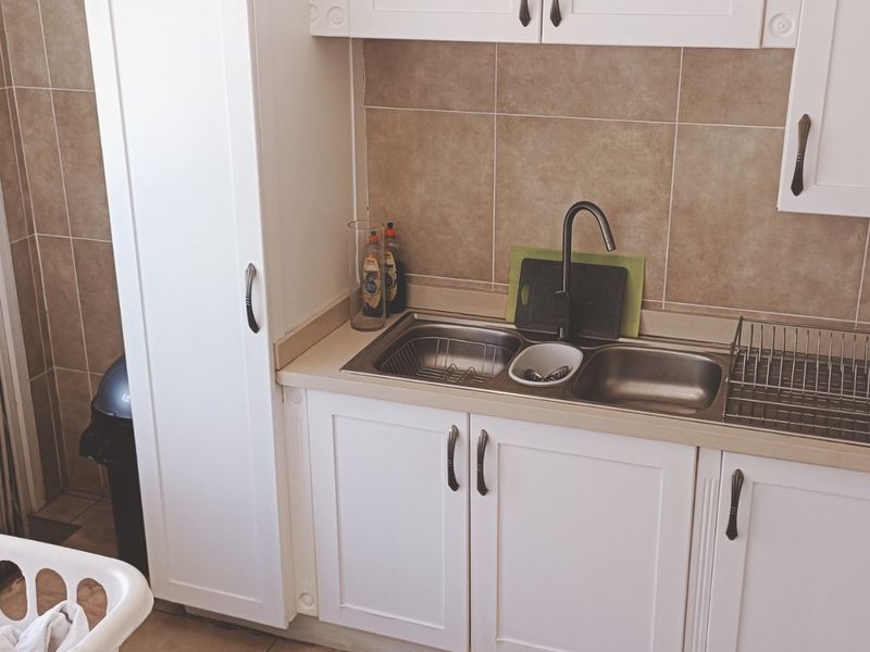 A functional laundry area featuring built-in cabinetry, a stainless steel double sink with mixer tap, and tiled splashback finishes.