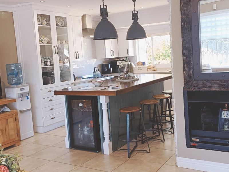 An open-plan living and kitchen area featuring a central island with a built-in wine cooler, white cabinetry, and a built-in fireplace.