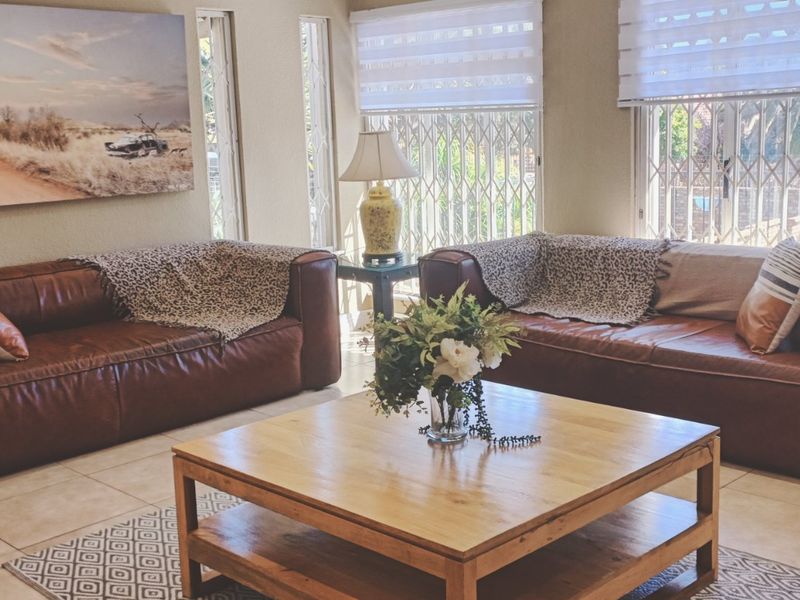 A comfortable living room featuring tiled flooring, secure window gates, and modern roller blinds, creating a bright and functional space.
